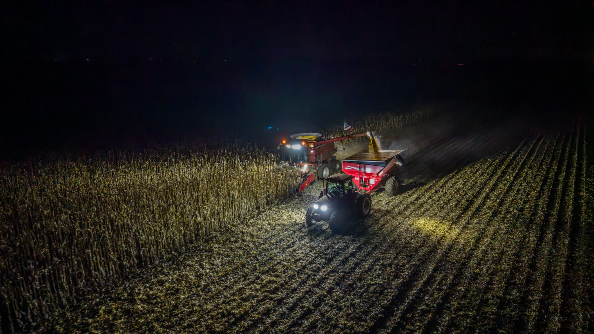 Nighttime aerial photography of farm equipment harvesting a cornfield